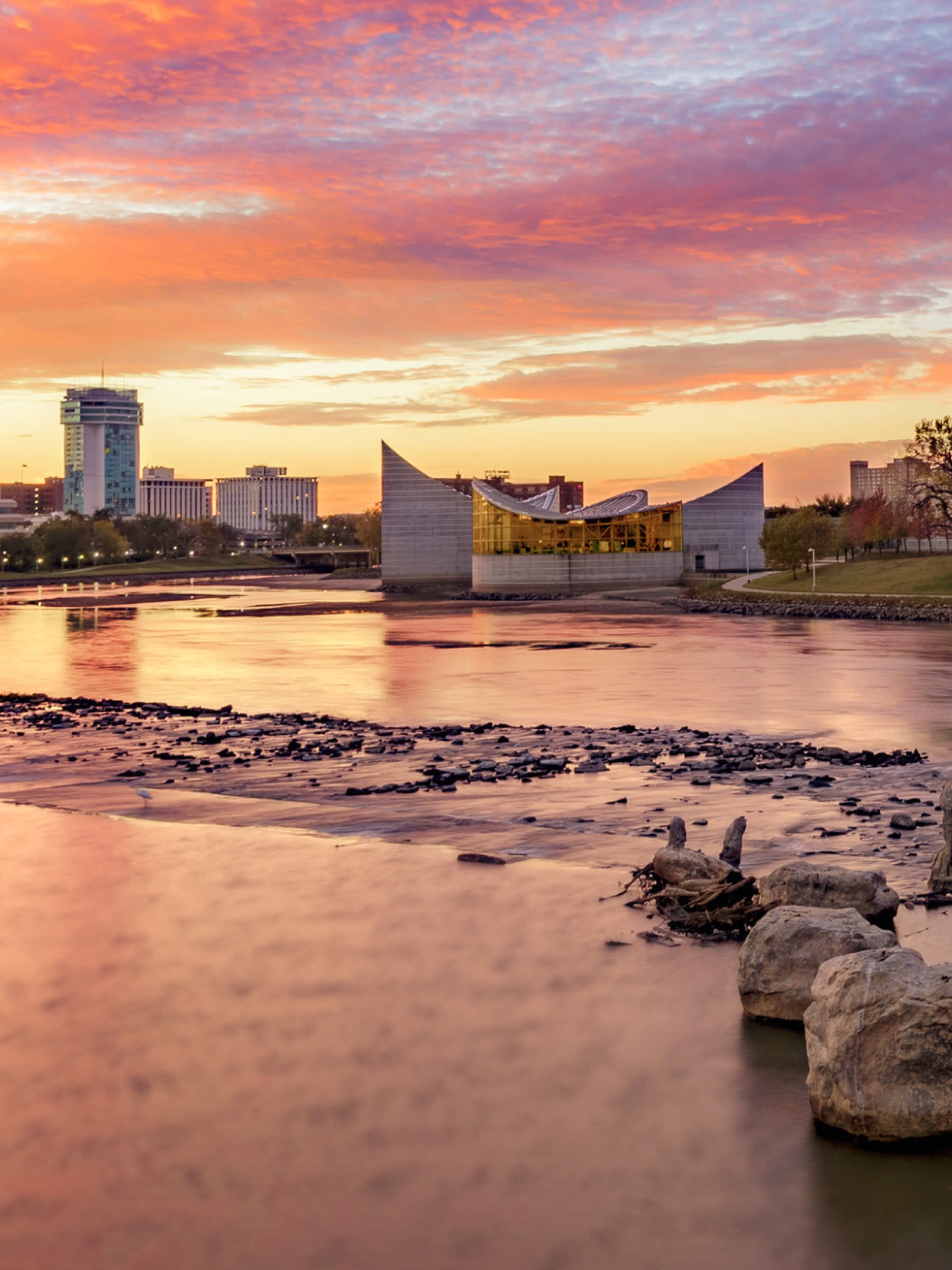 Sunset over Nashville, Tennessee, skyline with a river in the foreground, featuring the Schermerhorn Symphony Center and the AT&T Building in the background.