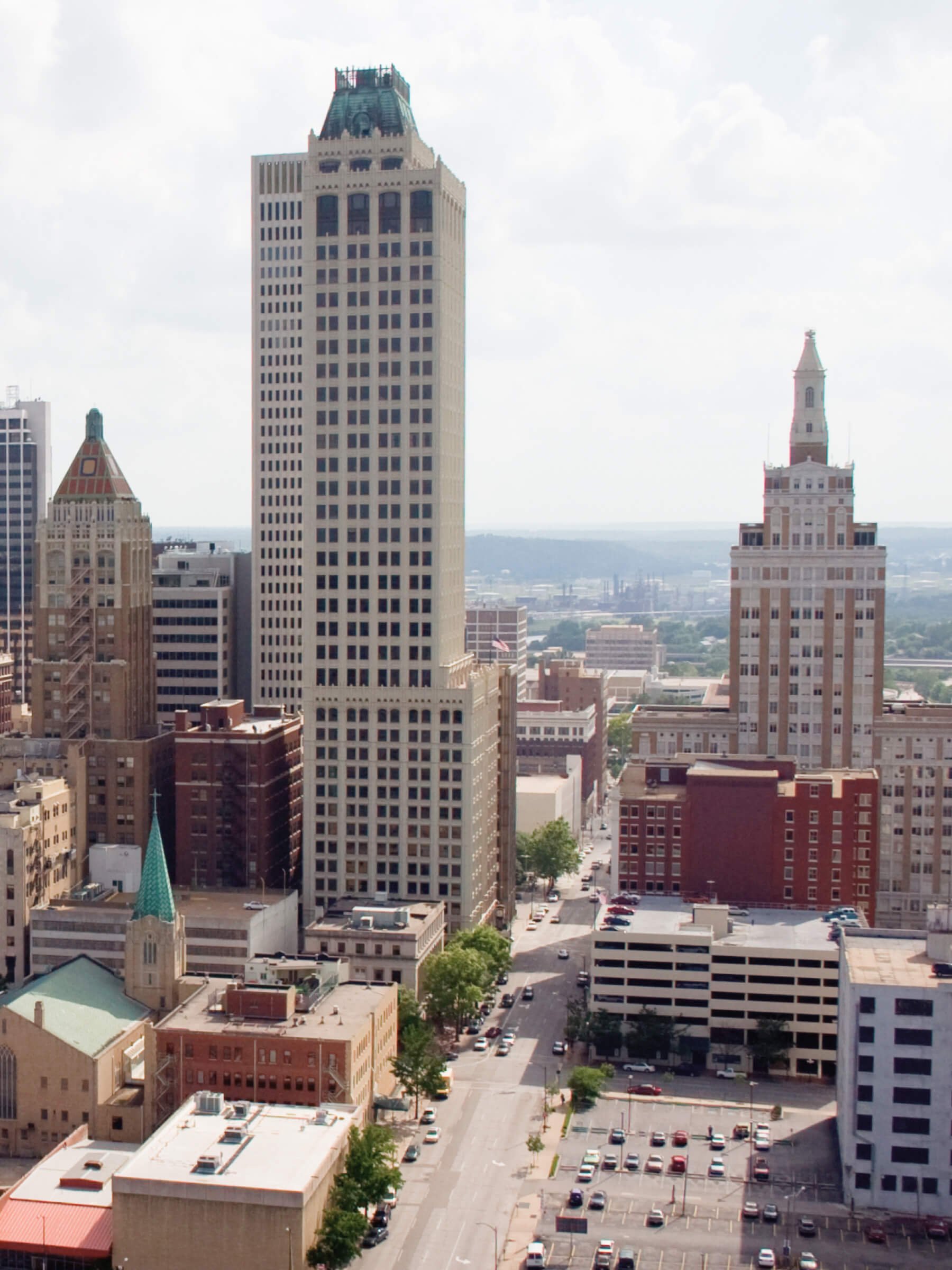 Tulsa, Oklahoma skyline with tall skyscrapers, including a prominent beige building with a green ornate top and another with a distinctive spire, visible from a high vantage point.