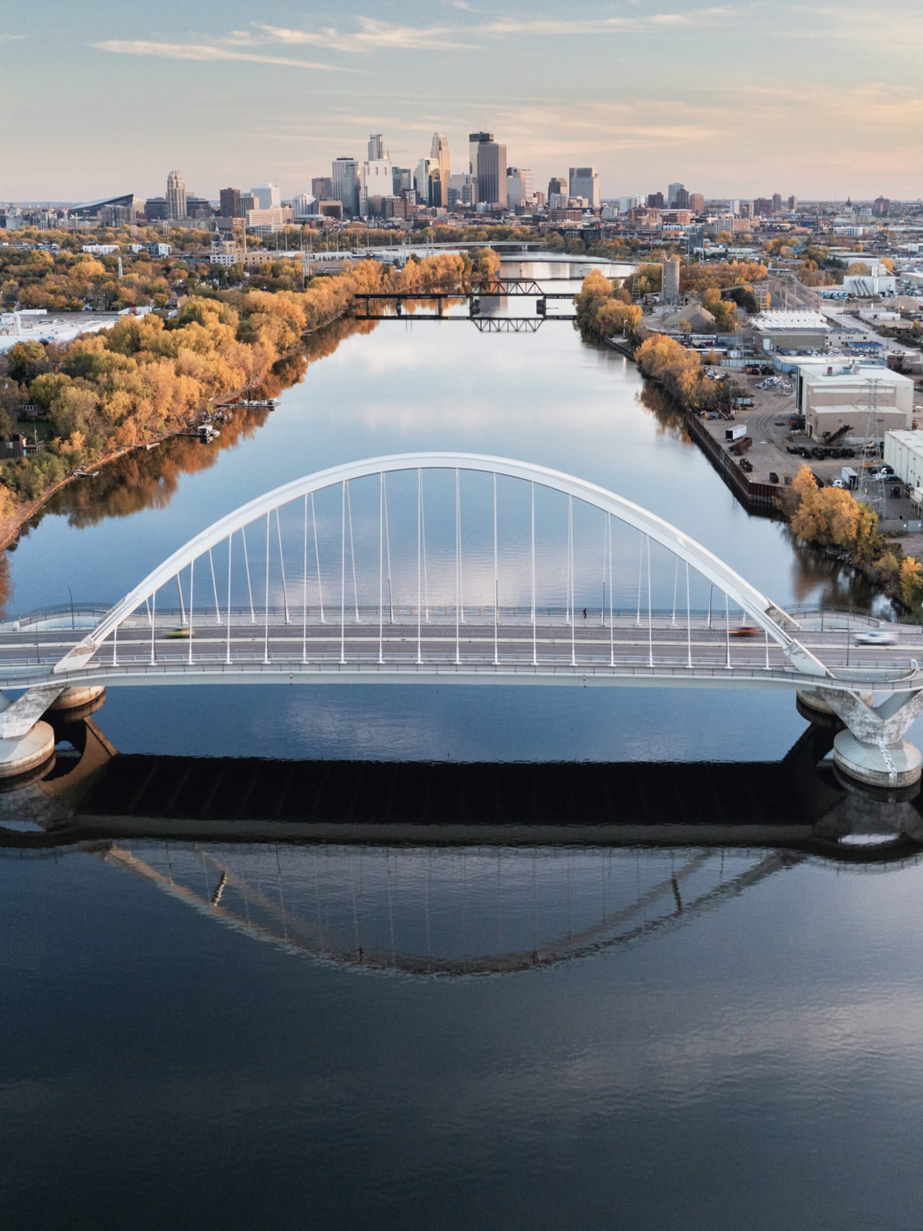 Aerial view of a city skyline with a river running through it, featuring a modern white arch bridge.