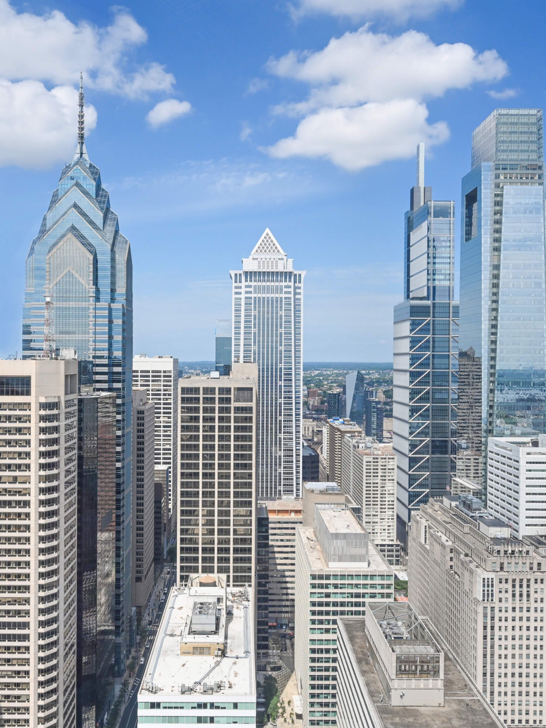 A cityscape with tall skyscrapers, including the Liberty Place buildings, under a partly cloudy blue sky.