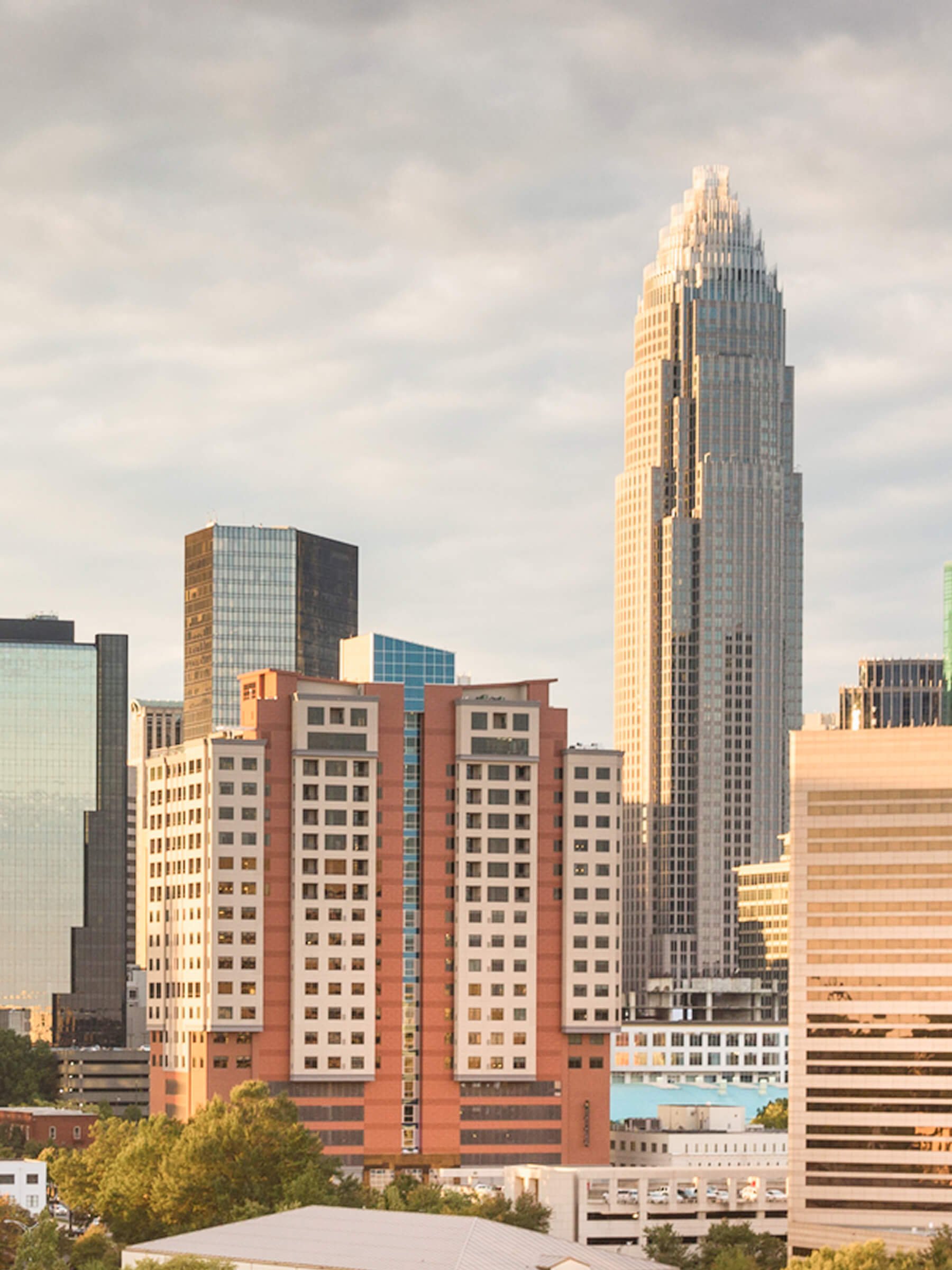 City skyline with tall buildings, including a prominent Art Deco skyscraper, under a partly cloudy sky.