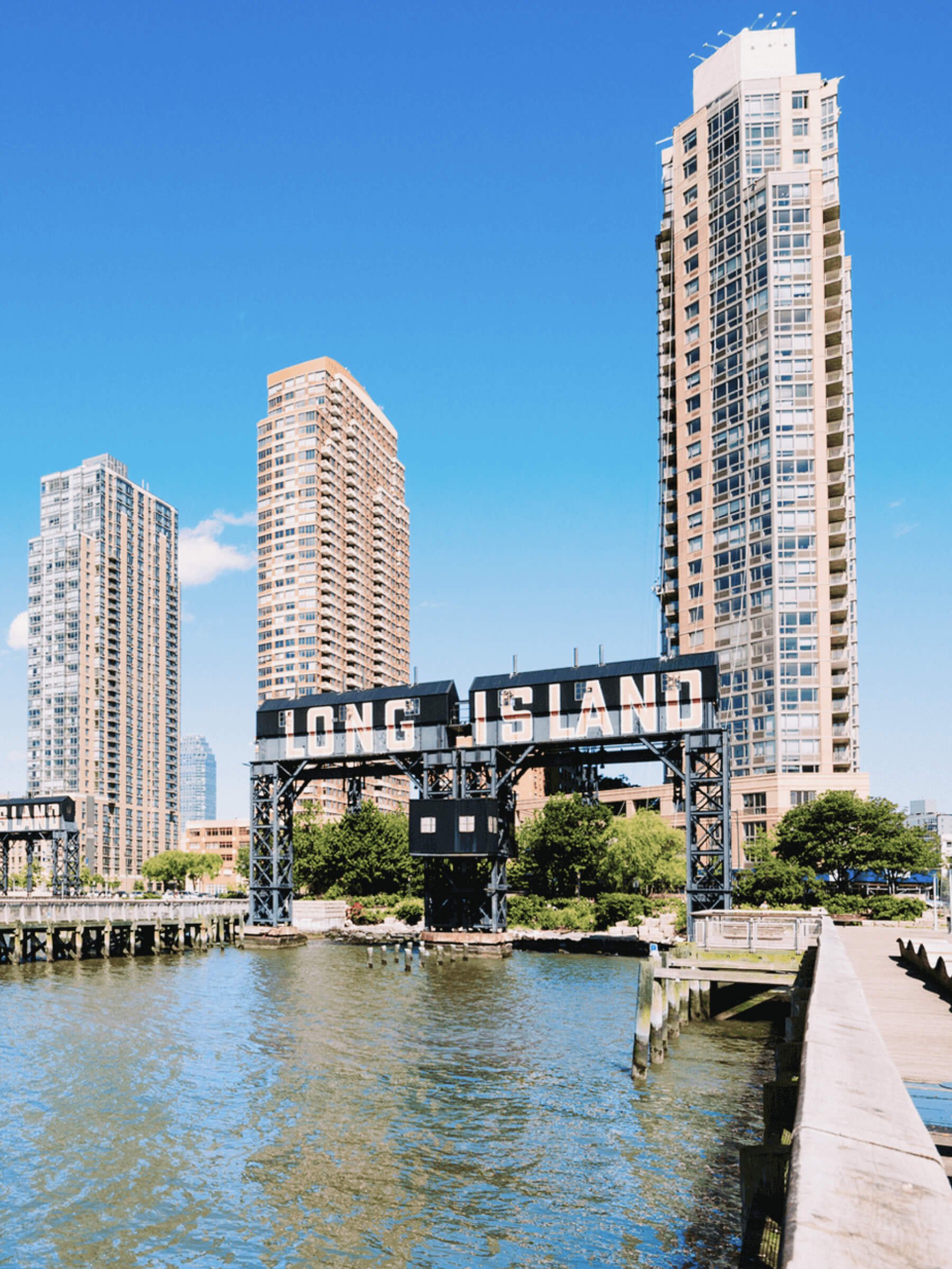Cityscape of Long Island City with water, tall buildings, and a sign that reads 'Long Island' in the foreground.
